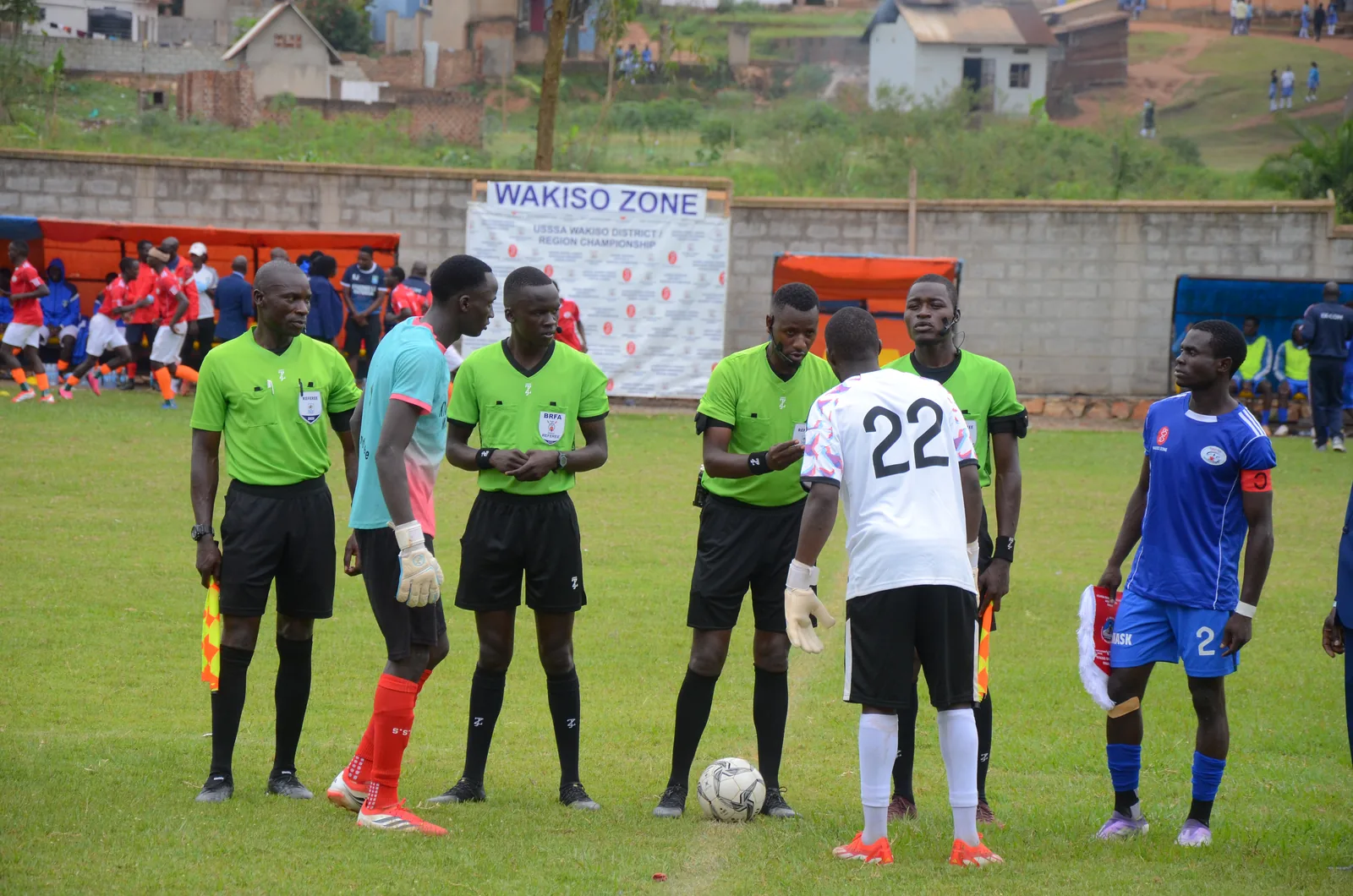 Referees and team captains gather around the match ball for the coin toss before a grassroots football match in Uganda